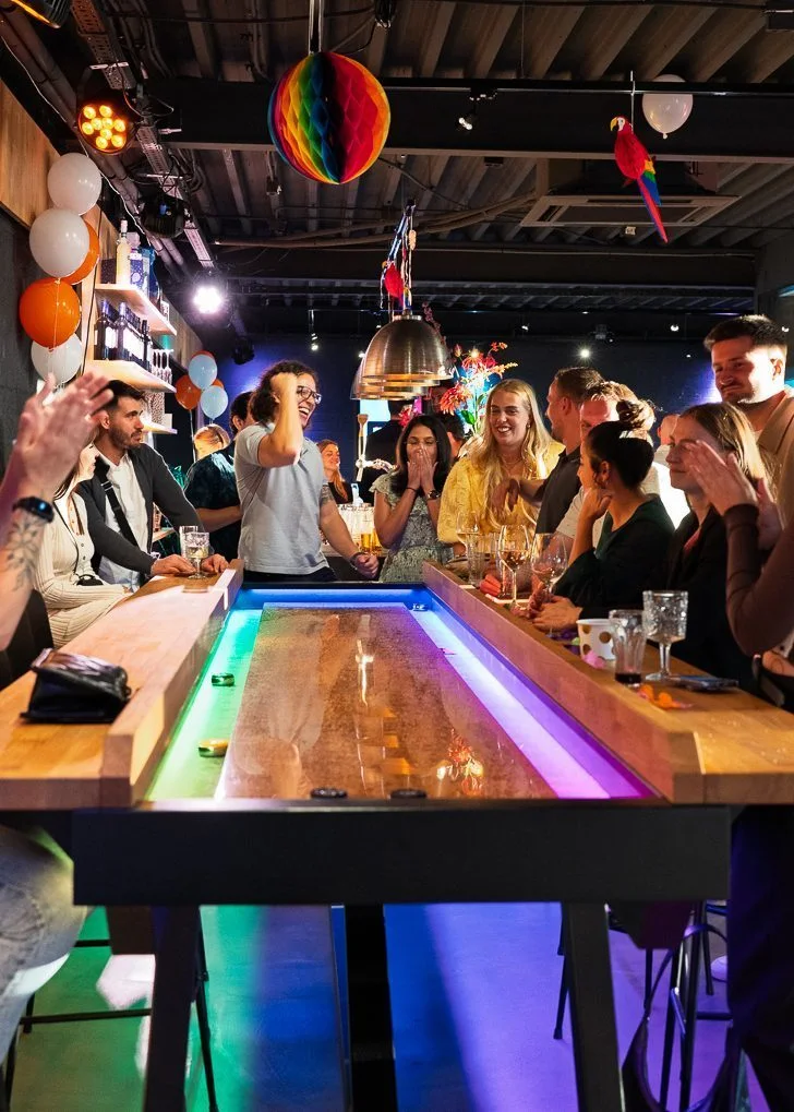 Friends celebrating around an interactive shuffleboard table